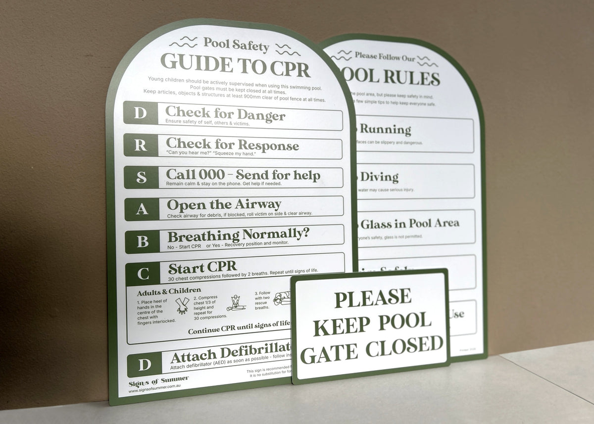Arched CPR pool safety guide signs with in pesto green, showing steps for CPR and pool rules, with a smaller sign reading 'PLEASE KEEP POOL GATE CLOSED' in front, photographed against a beige wall.